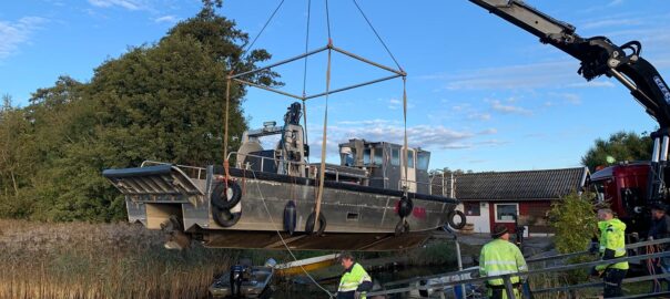 Trålbåten Östen lyfts ner i Ringsjön av en kranbil. Skeppare och däckshänder hjälper till med sjösättningen.