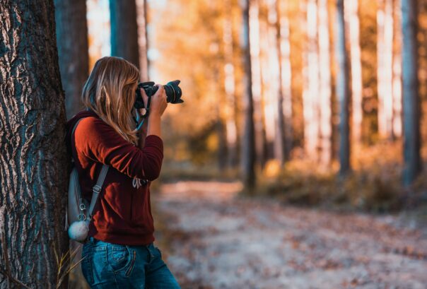 Person i skog som står och tar bild med en kamera.